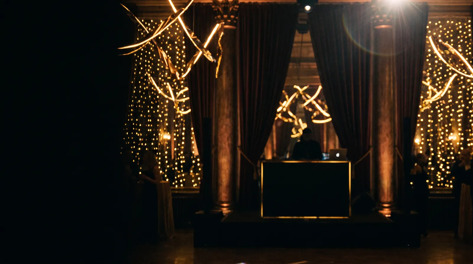 Elegant black and gold event reception with warm golden light and a DJ booth silhouette