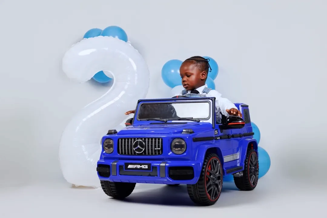 Toddler sitting in a toy car beside a number-two balloon for a 2nd birthday shoot