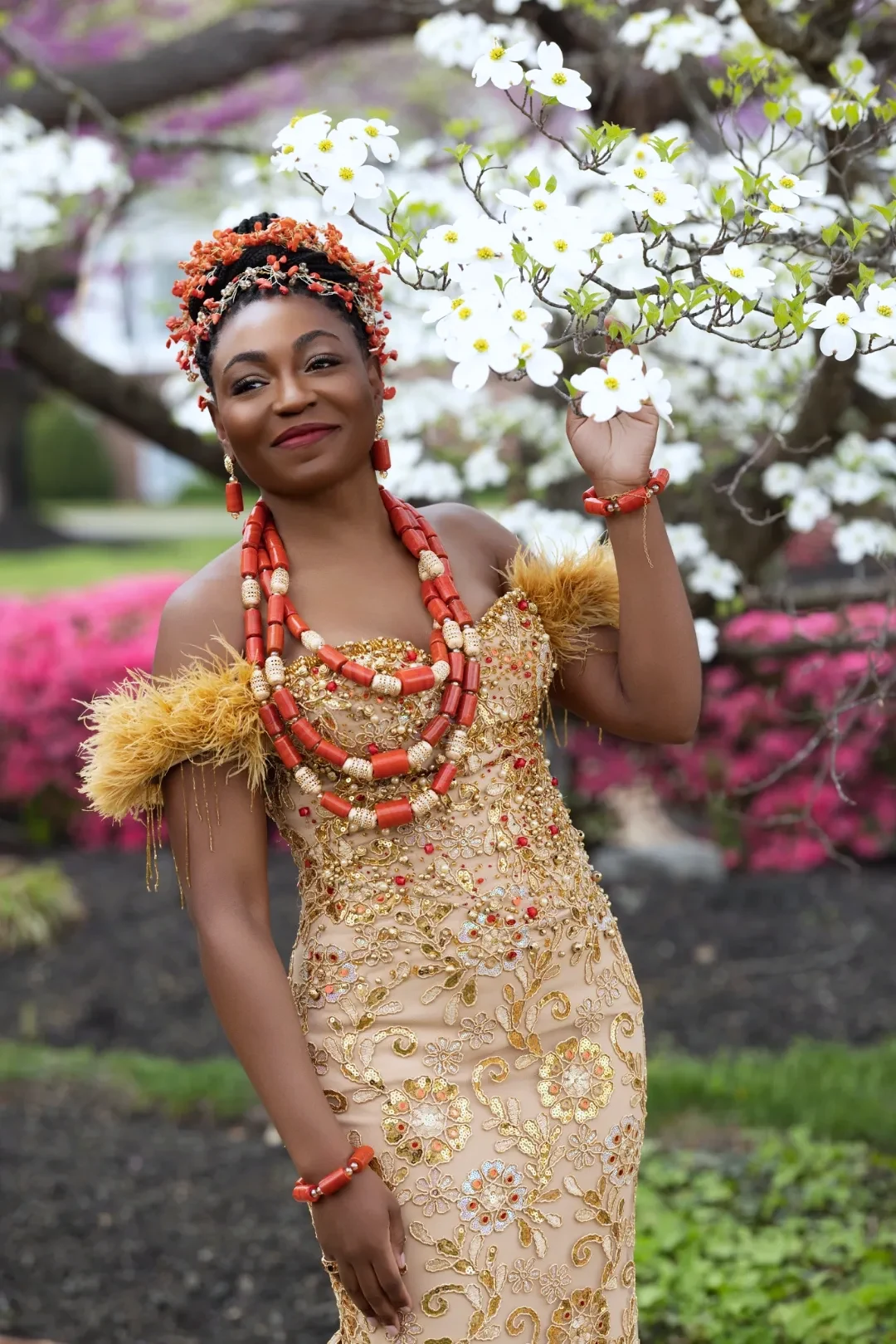 Bride in traditional Nigerian coral bead regalia and gold lace gown among spring blossoms