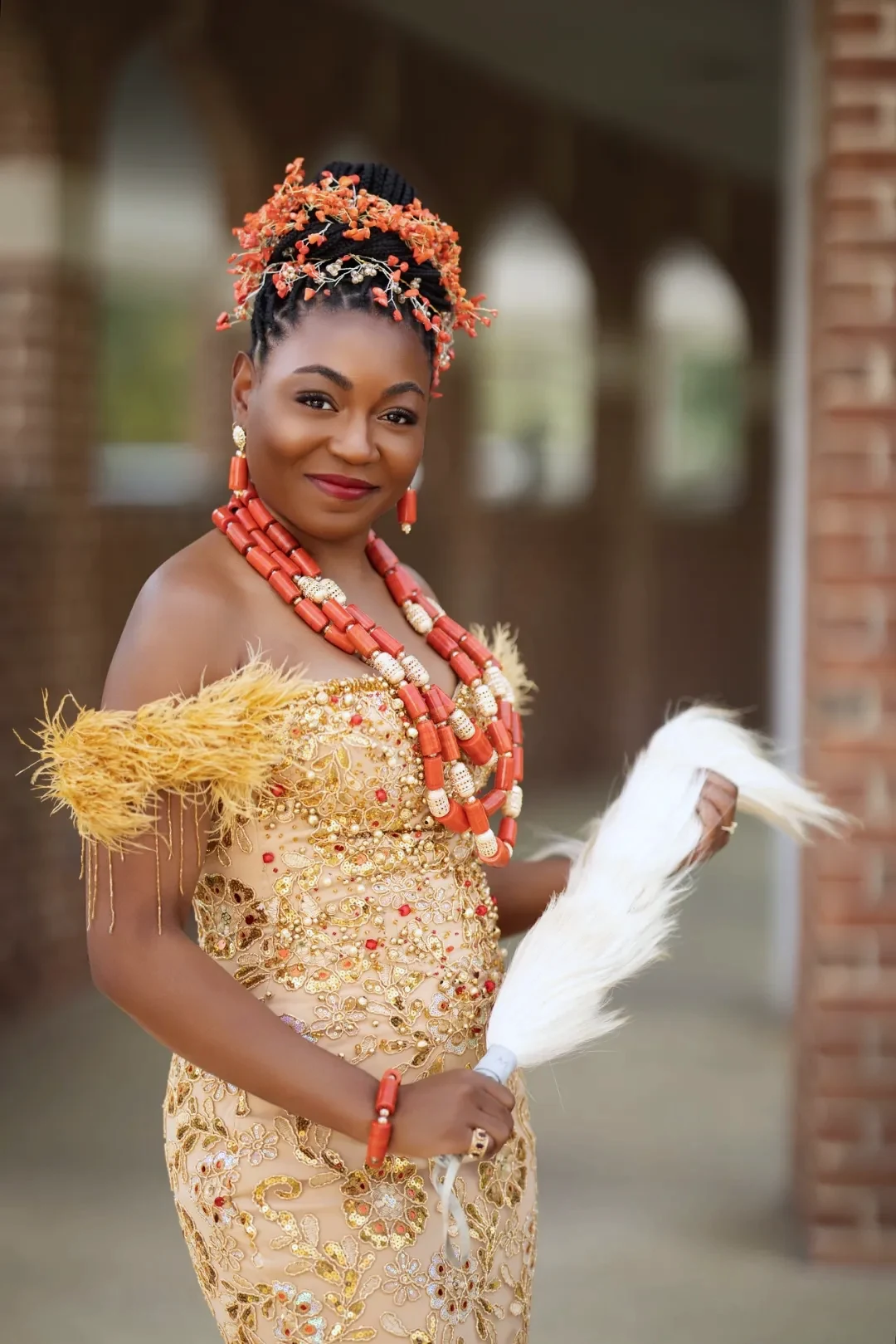 Traditional bridal portrait with coral beads and horsetail fan under a covered walkway