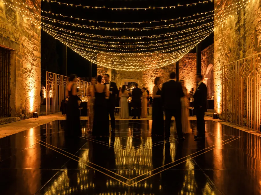 Guests dancing on a reflective black dance floor beneath draped string lights