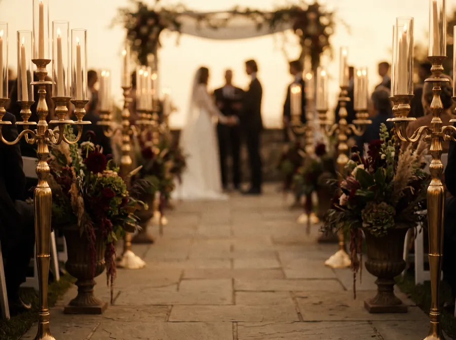 Wedding ceremony aisle lined with gold candelabras and dark floral arrangements