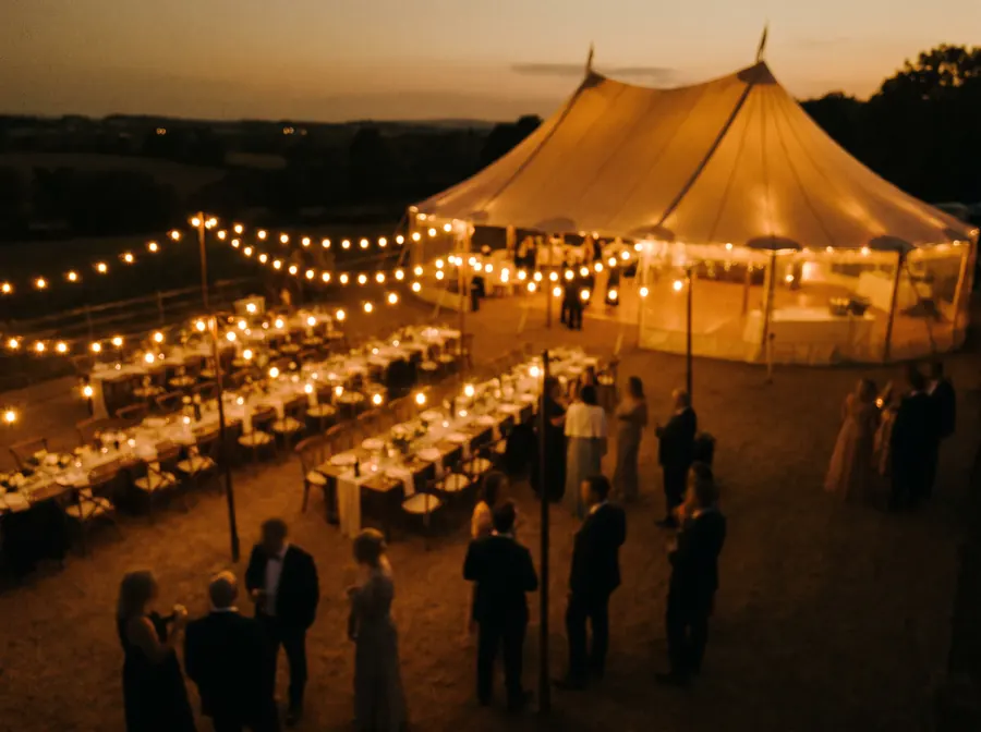 Aerial film-style still of an outdoor event venue at dusk with string lights